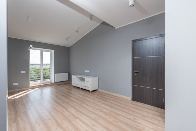 Empty modern room with light wood flooring, grey walls, and balcony access.
