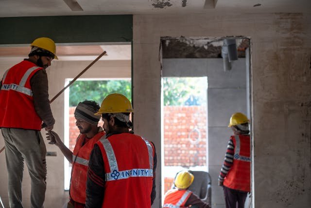 Construction workers in red vests and hard hats working indoors on-site.
