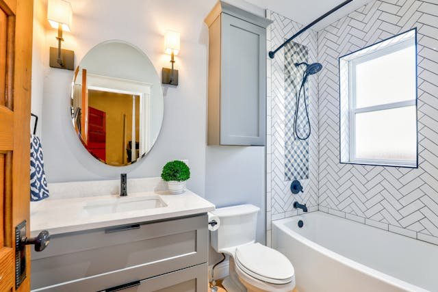 Compact bathroom with herringbone tiles, grey vanity, and wall sconces.