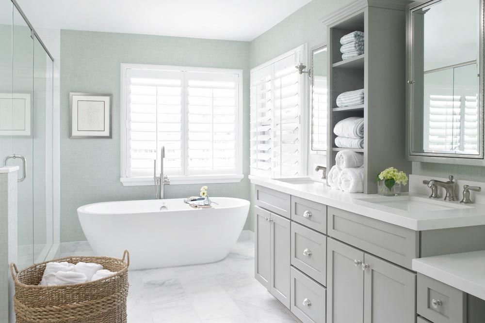 Airy bathroom with freestanding tub, plantation shutters, and double vanity.