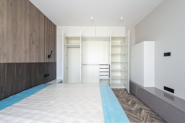 Minimal bedroom with chevron flooring and open white wardrobe storage system.