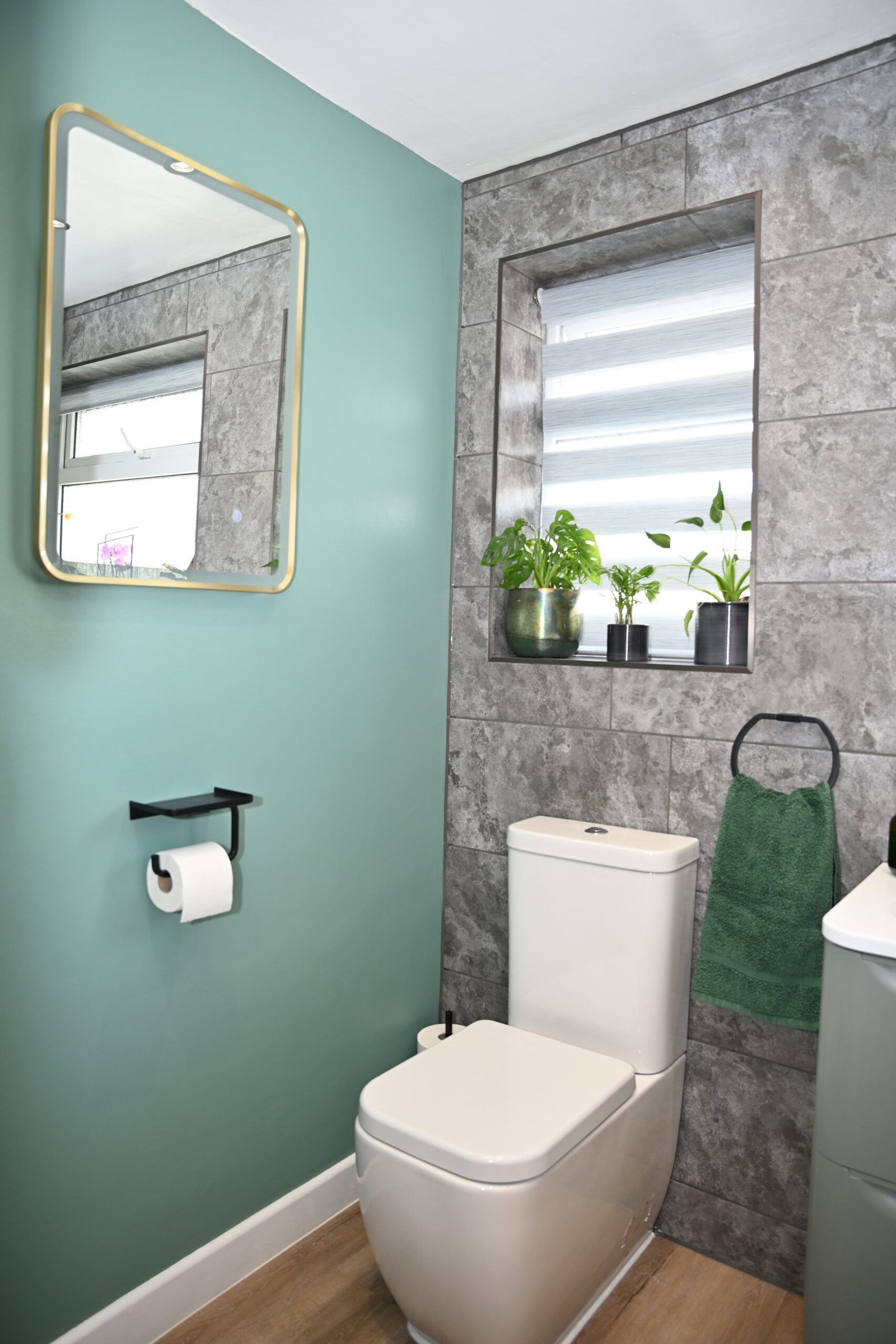 Toilet with green towel and plants on tiled window sill near mirror.