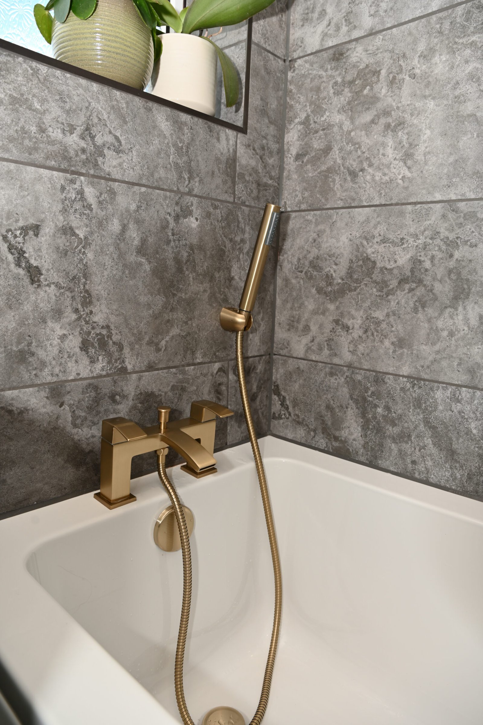 Close-up of bathtub with brushed brass faucet and handheld showerhead.