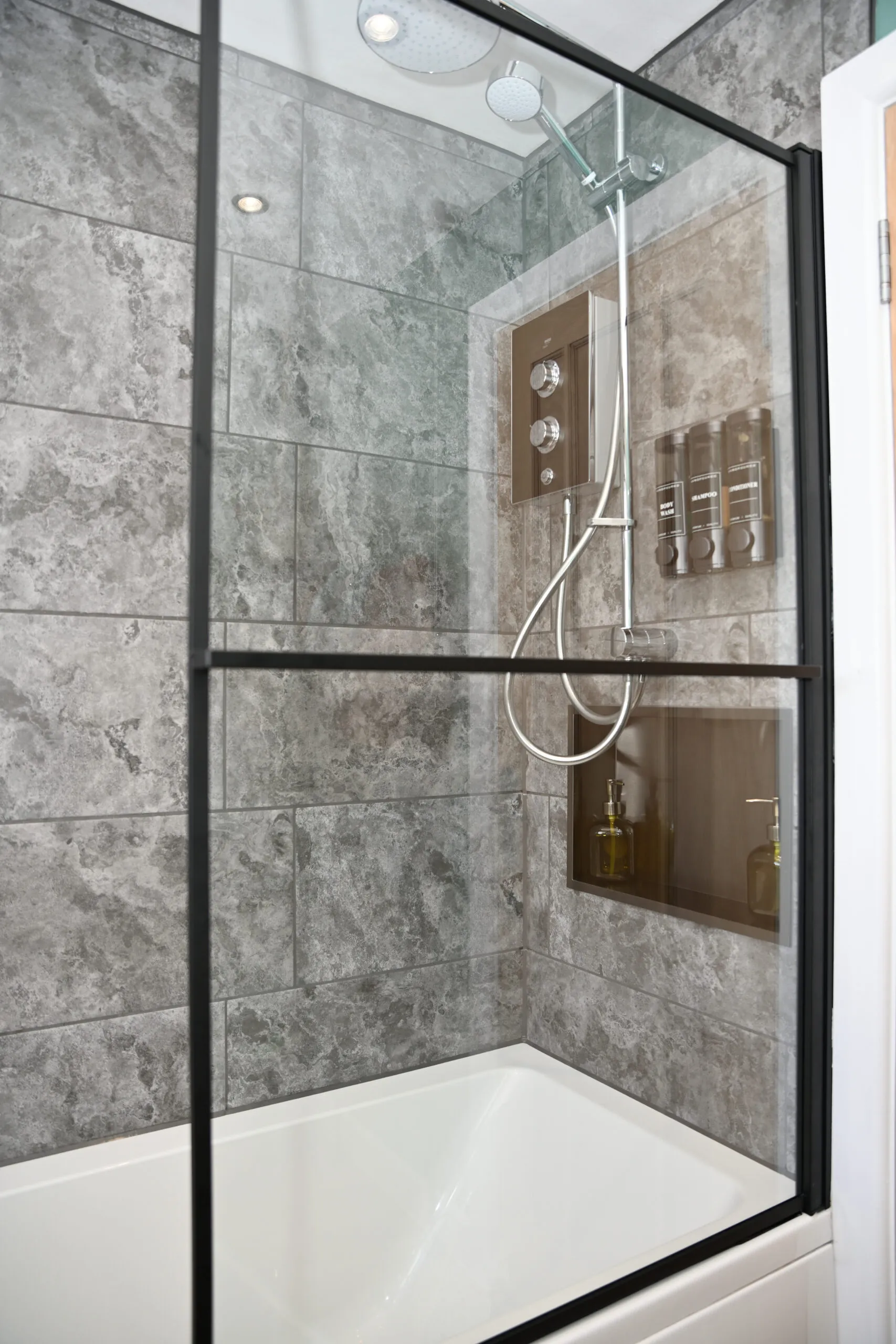 Modern shower area with rainfall head, glass screen, and built-in shelf.